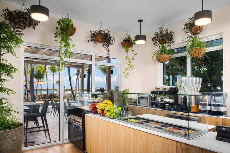 Coastal kitchen with hanging plants, white cabinetry, fresh fruit bowl, and ocean view through sliding glass doors