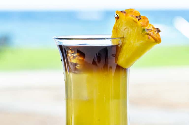 Tropical cocktail with pineapple garnish against beach and ocean backdrop