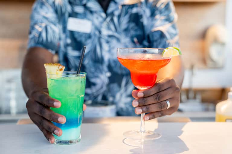 Person holding colorful tropical cocktails with lime and pineapple garnish