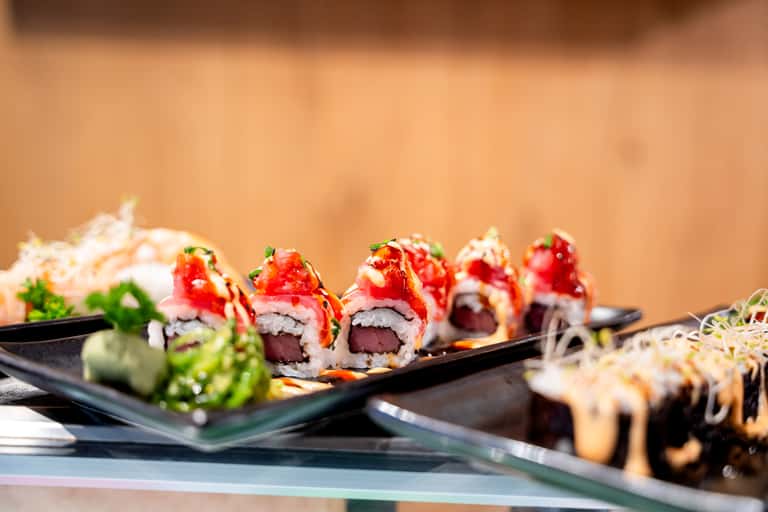 Plated sushi rolls with red topping, cucumber, and garnish on black slate plate