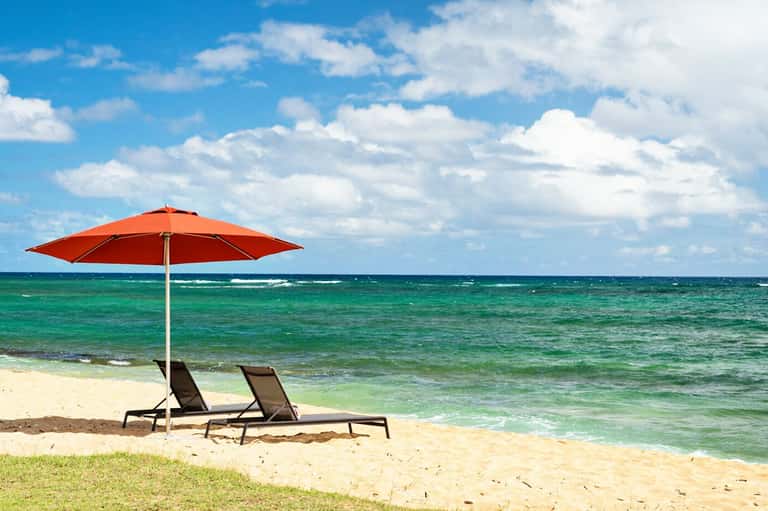Red umbrella and lounge chairs on a sandy beach overlooking turquoise ocean