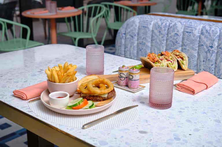 Outdoor dining setup with burger, onion rings, fries, and tacos on marble table