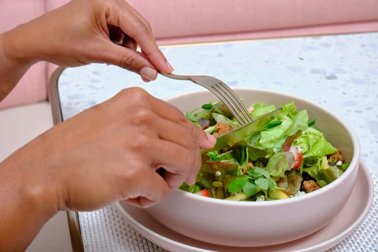 Person eating fresh green salad with croutons from pink bowl at outdoor restaurant