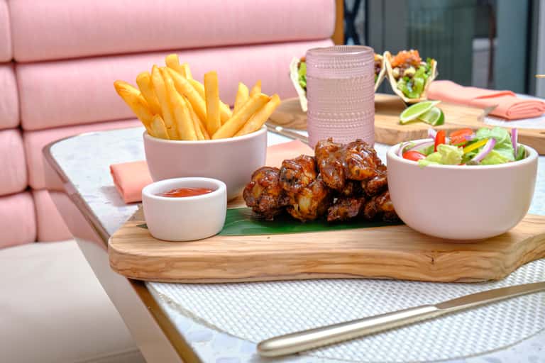 Wooden board with fries, glazed chicken pieces, and mixed salad on marble table