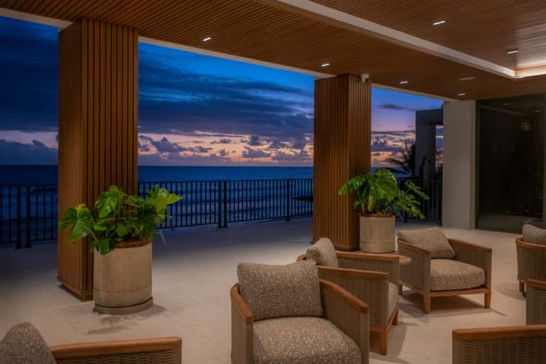 Modern beachfront terrace at dusk with wooden columns, lounge chairs, and ocean view