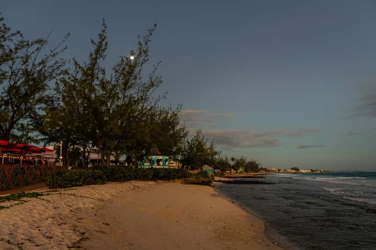 Sandy beach with colorful beachfront restaurants and trees under evening sky