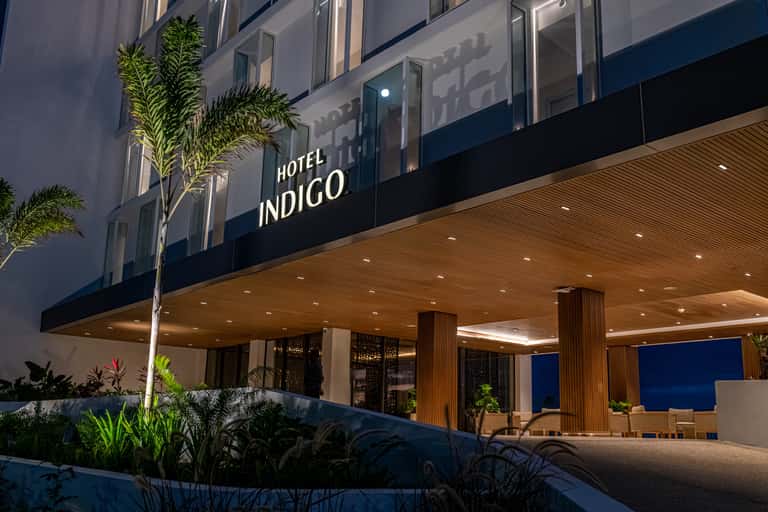 Hotel Indigo entrance at night with modern signage, tropical plants, and ocean view