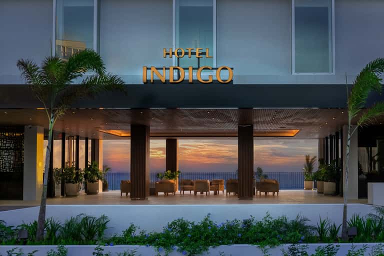 Hotel Indigo beachfront entrance at dusk with golden lighting, ocean views, and covered terrace seating