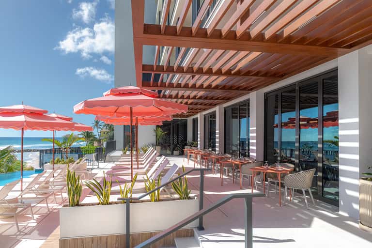 Beachfront terrace with red umbrellas, lounge chairs, wooden pergola, and ocean view during daytime