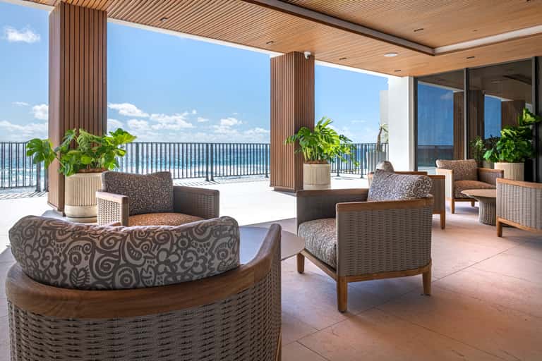 Upscale lounge area with woven furniture, wooden columns, ocean views, and potted plants on covered deck