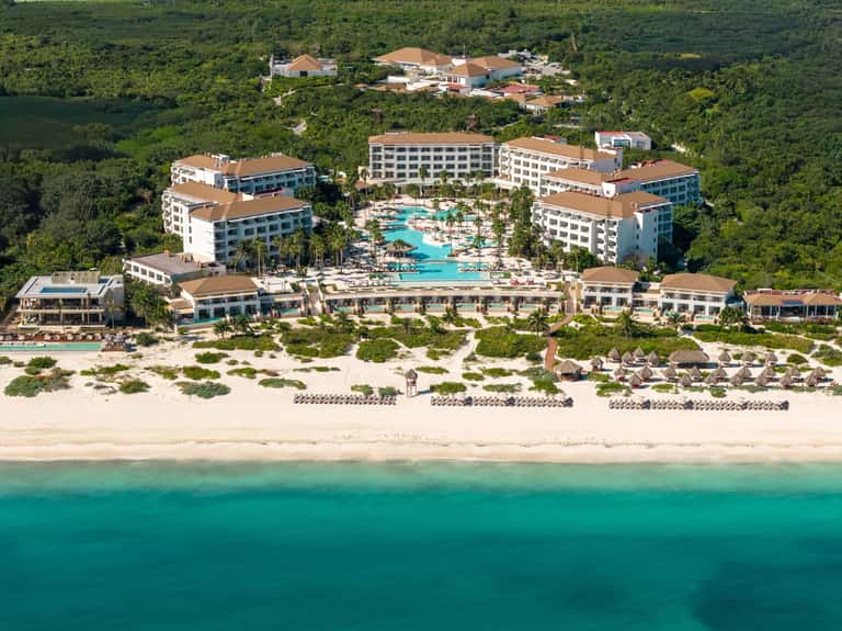 Aerial view of beachfront resort with multiple buildings, turquoise pool, beach, and surrounding tropical forest