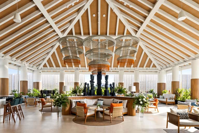 Modern hotel lobby with high wooden ceiling, geometric skylights, chandelier, and casual seating areas