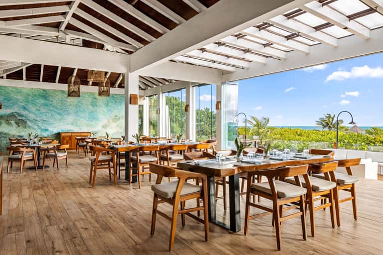 Modern dining room with wooden tables, pendant lights, skylight ceiling, ocean and landscape views