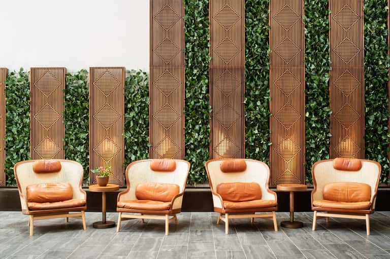 Four modern chairs with cognac leather cushions against geometric wood wall