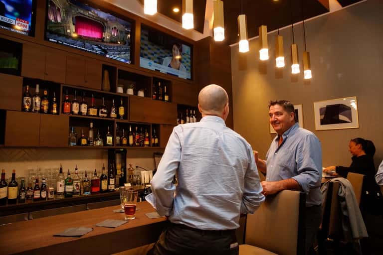 Upscale bar interior with extensive liquor collection and two men conversing at counter