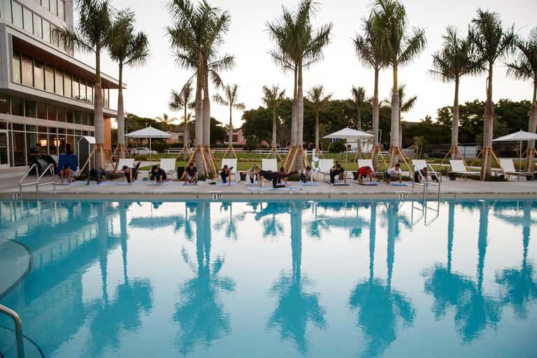 Resort pool with palm trees, lounge chairs, umbrellas, and modern building facade