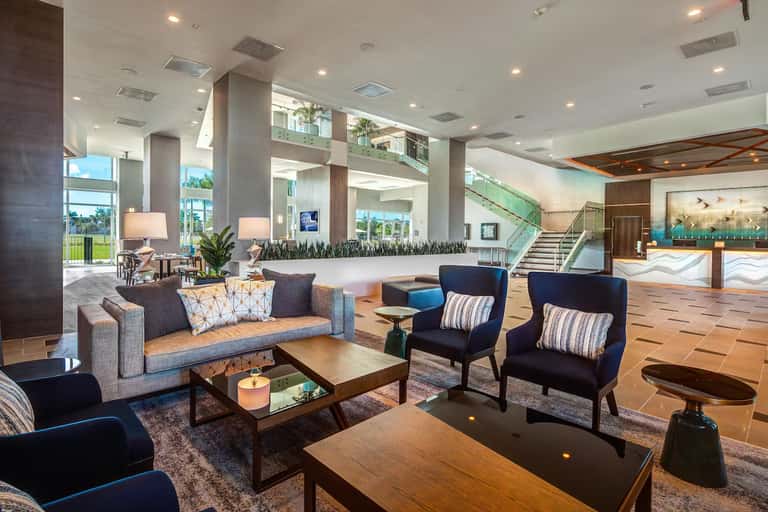 Spacious hotel lobby with high ceilings, modern furniture, columns, and outdoor views