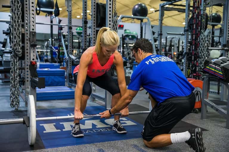 Personal trainer assisting woman with weightlifting in well-equipped gym facility