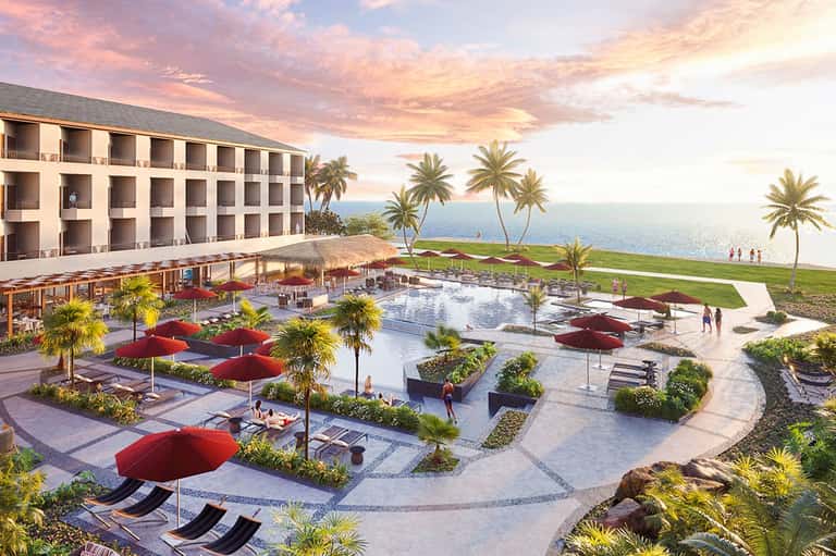 Beachfront resort at sunset with oceanview pool, palm trees, red umbrellas, and multi-story hotel building