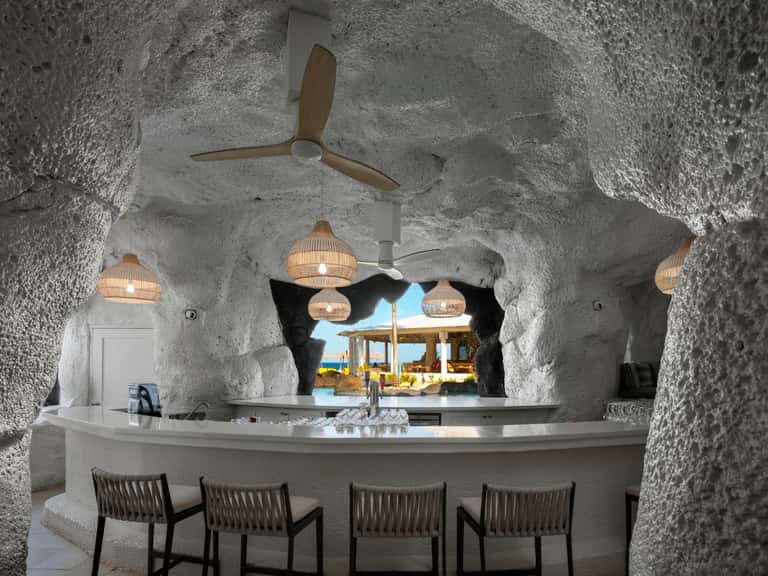 Modern beach bar with white stone walls, hanging pendant lights, and ocean view
