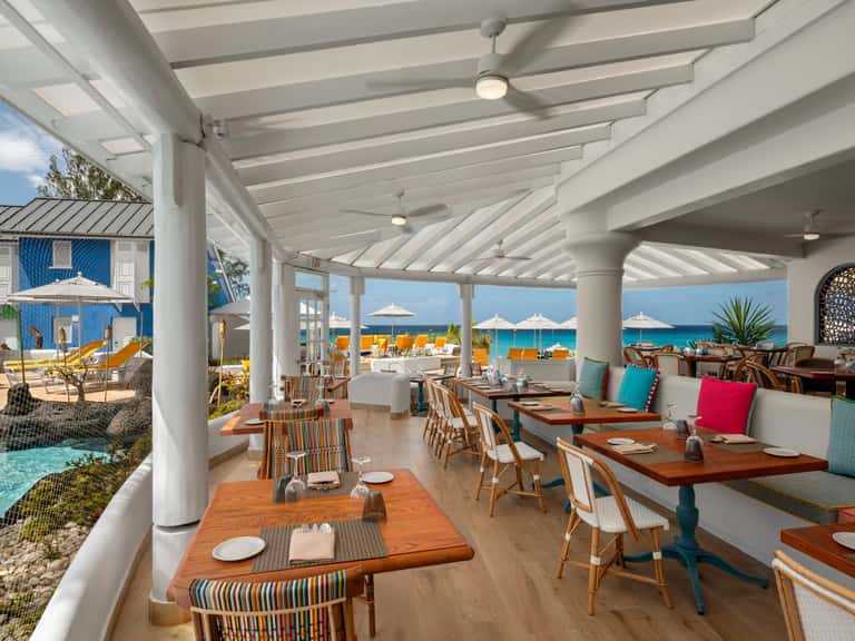 Modern beachfront restaurant with wooden tables, white columns, and ocean views through glass walls
