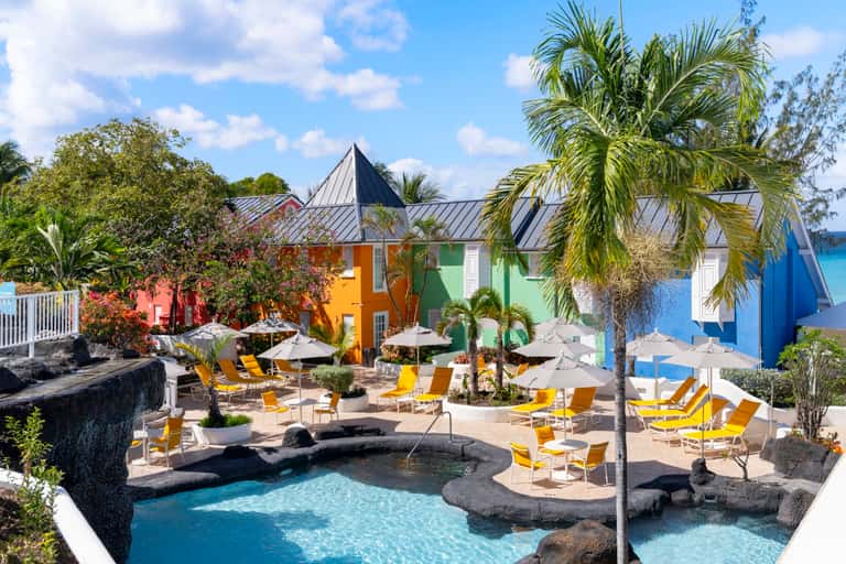 Colorful resort buildings with yellow loungers around a natural stone pool surrounded by palm trees
