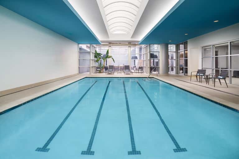 Indoor lap pool with lane markers, teal ceiling, and seating area overlooking city