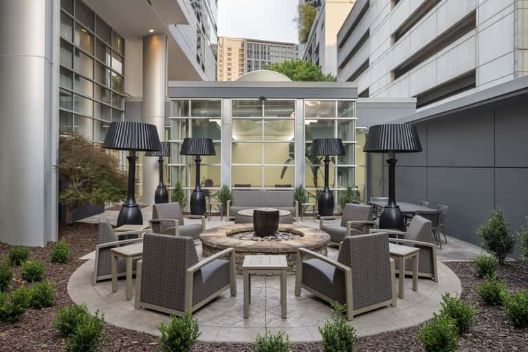 Outdoor courtyard fire pit surrounded by woven chairs with black heat lamps