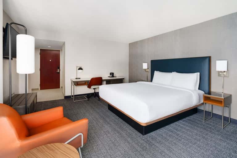 Contemporary hotel room with blue headboard bed, orange sofa, and modern furnishings