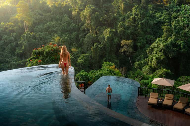 Infinity pool overlooking dense forest canopy with guests swimming at luxury jungle resort
