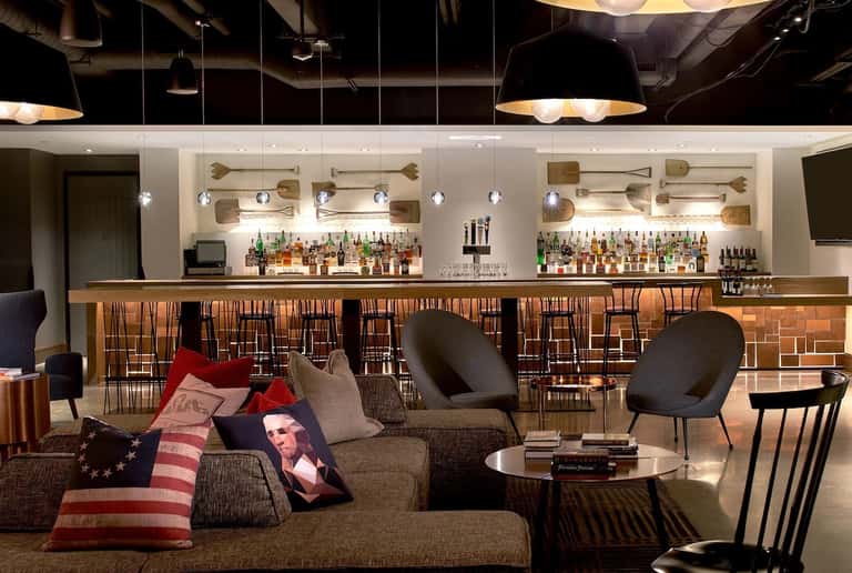 Modern lounge with brown leather bar seating, extensive liquor display, and contemporary pendant lighting