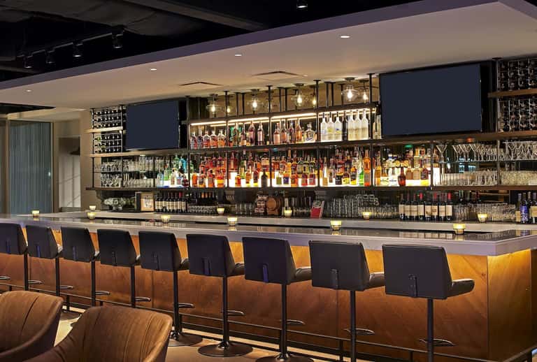 Upscale bar interior featuring illuminated shelving with spirits bottles and amber-toned bar seating