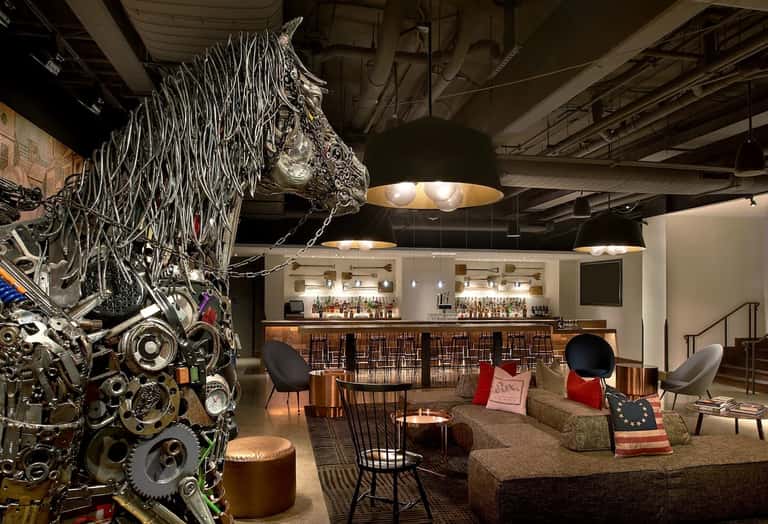 Industrial-style bar lounge with sculptural metal horse artwork, brick elements, and modern furnishings