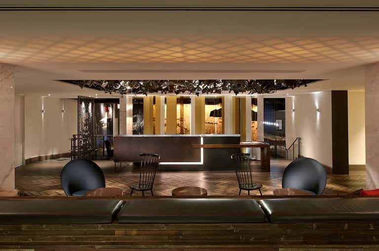Minimalist hotel lobby featuring sculptural black art installation, illuminated reception desk, and clean lines