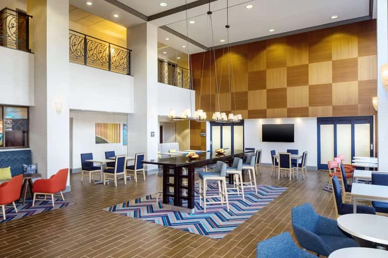Multi-story hotel atrium lobby with gold wood accents, dining tables, lounge seating, and modern architecture