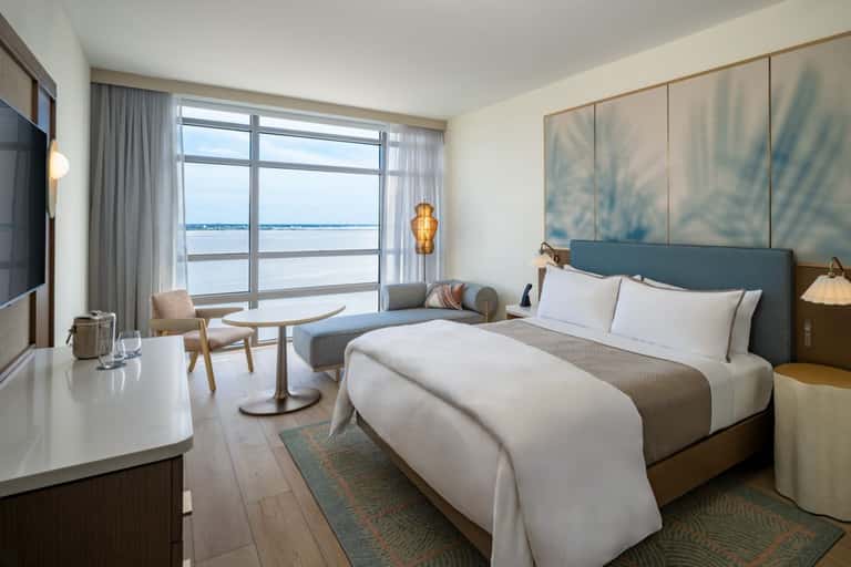 Luxury hotel bedroom with ocean view balcony, modern furnishings, and floor-to-ceiling windows