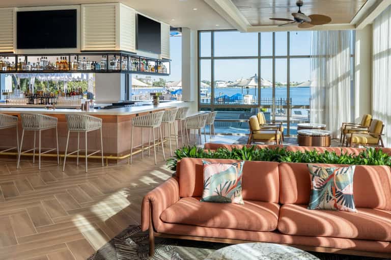 Hotel lounge with coral sofa, full bar, large windows overlooking blue water and boats