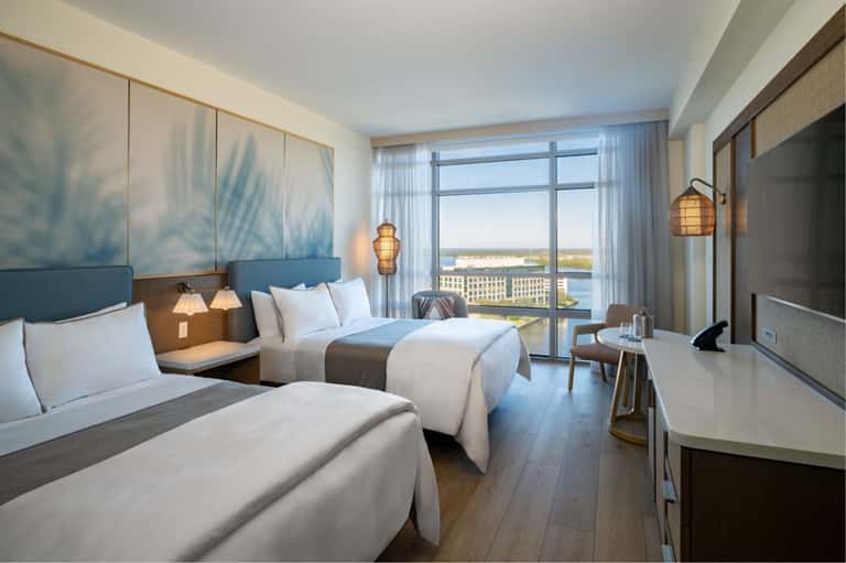 Hotel room with two queen beds, blue headboard, waterfront view, and modern decor