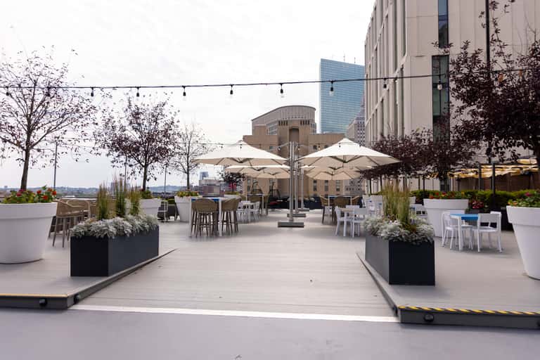 Urban rooftop lounge with white umbrellas, dining tables, and city skyline backdrop
