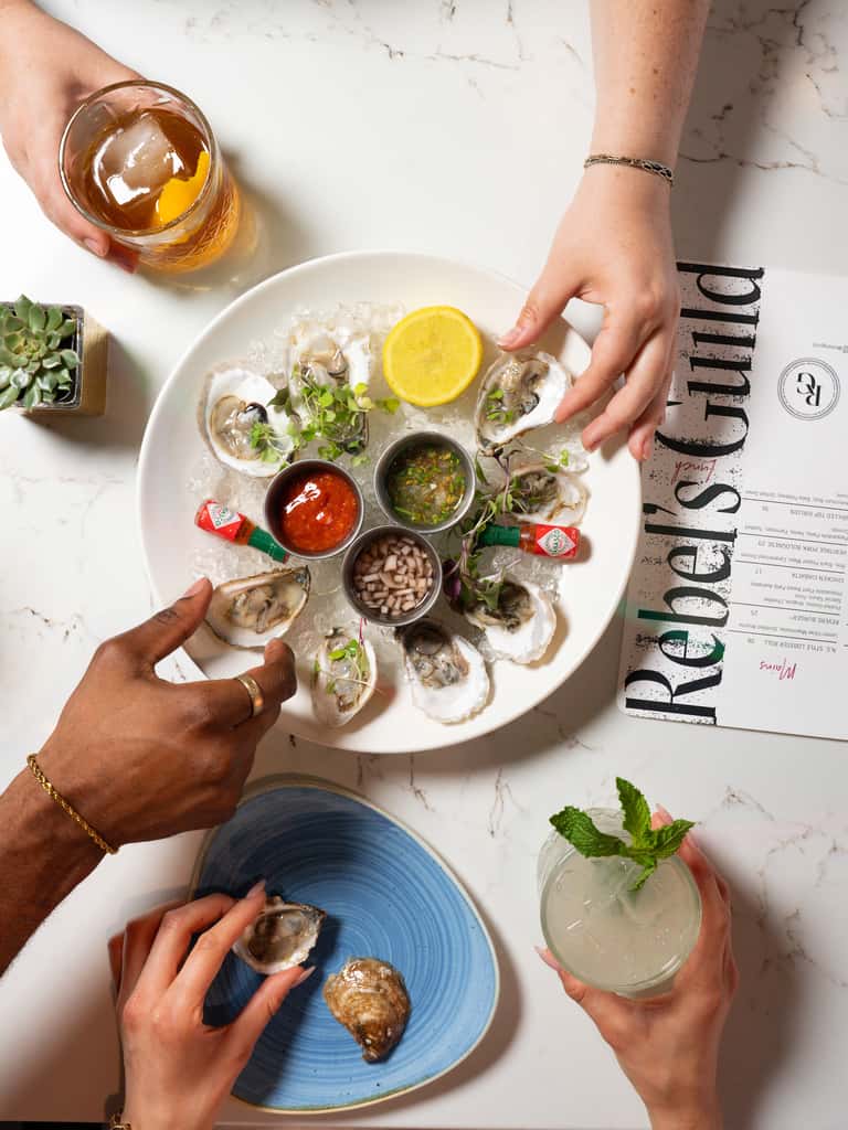 Oyster platter with lemon, sauces, and garnishes arranged on white plate with cocktails