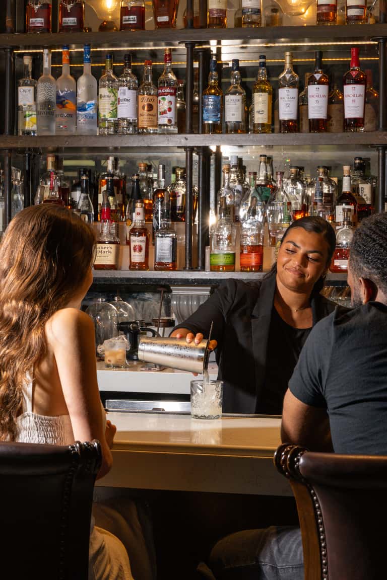Bartender preparing drinks behind bar with extensive spirit bottle collection