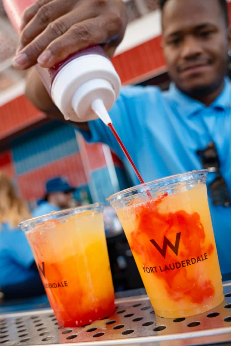 Hands pouring red syrup into tropical cocktails marked with Fort Lauderdale branding