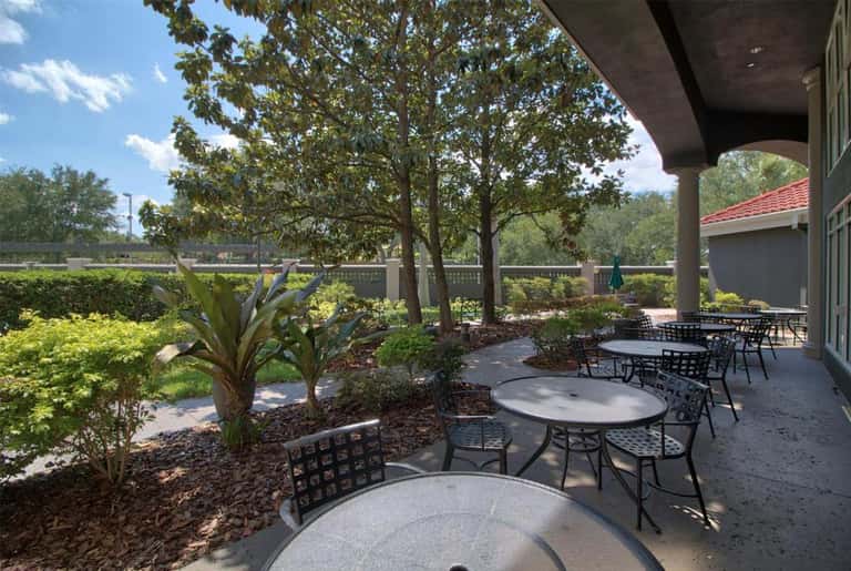 Shaded terrace patio with round tables, black chairs, and manicured garden landscape
