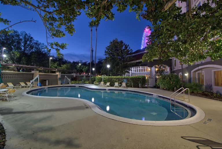 Illuminated resort pool at dusk with lounge chairs, surrounded by landscaping and buildings