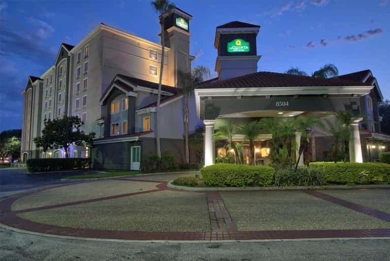 La Quinta hotel exterior at twilight with illuminated entrance, tower signage, and landscaping