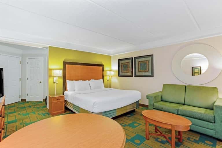 Spacious hotel suite with king bed, orange headboard, green sofa, and round mirror