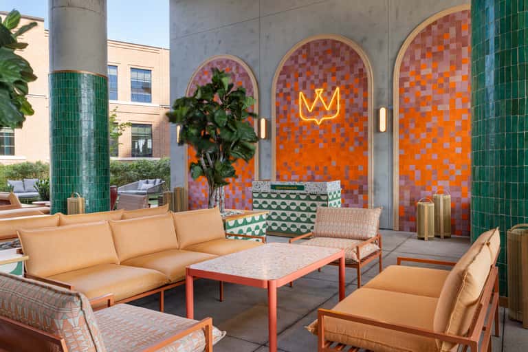 Contemporary outdoor lounge area with orange mosaic tile walls, neon crown sign, green columns, and modern seating