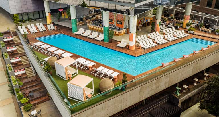 Aerial view of dual resort pools with wooden decking, lounge chairs, umbrellas, and colorful column art installations