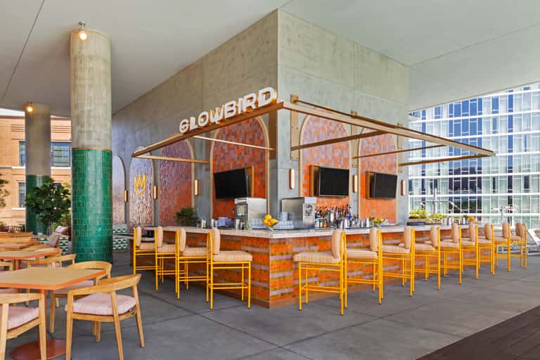 Indoor bar lounge with mosaic tile backsplash, orange decor, wooden chairs with striped cushions, and colorful art