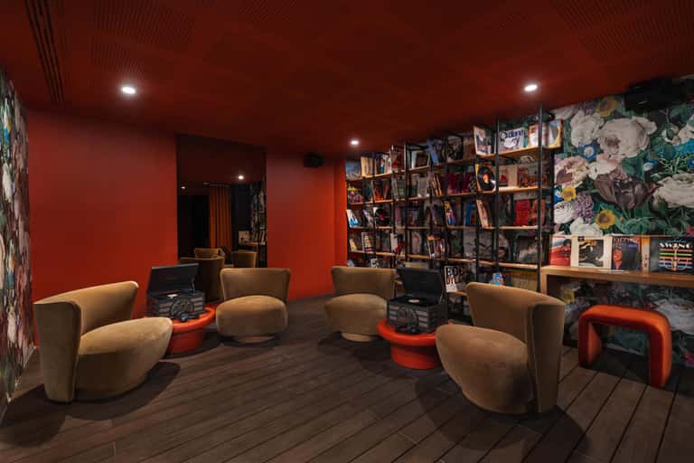 Modern library lounge with red walls, curved tan chairs, bookshelves, and decorative floral artwork